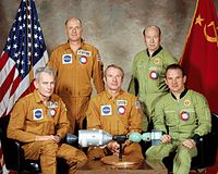 the five crew members of ASTP sitting around a miniature model of their spacecrafts