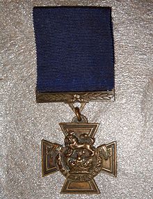 The obverse of the bronze cross patt&eacute;e medal; showing the crown of Saint Edward surmounted by a lion with the inscription FOR VALOUR with a blue ribbon